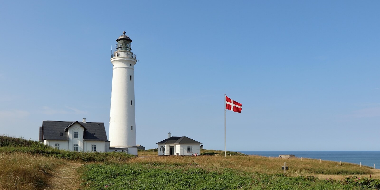 Dansk kystlandskab med fyr og Dannebrog — vind og vejr præger elproduktionen Dansk kystlandskab med fyr og Dannebrog — vind og vejr præger elproduktionen
